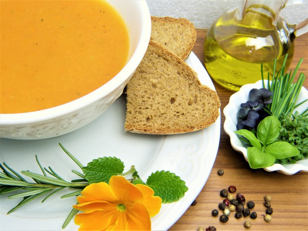 A bowl of carrot soup on a plate with wholemeal bread