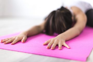 A young woman lies in child's pose on a pink yoga mat
