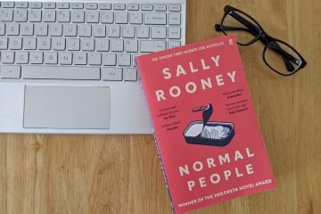 The book Normal People rests on a desk next to a silver laptop and a pair of black glasses
