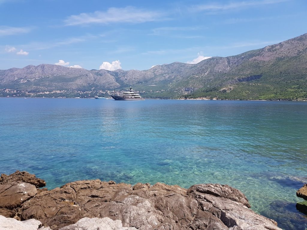 A rocky outcrop looking out to cystal clear, blue water with a small boat