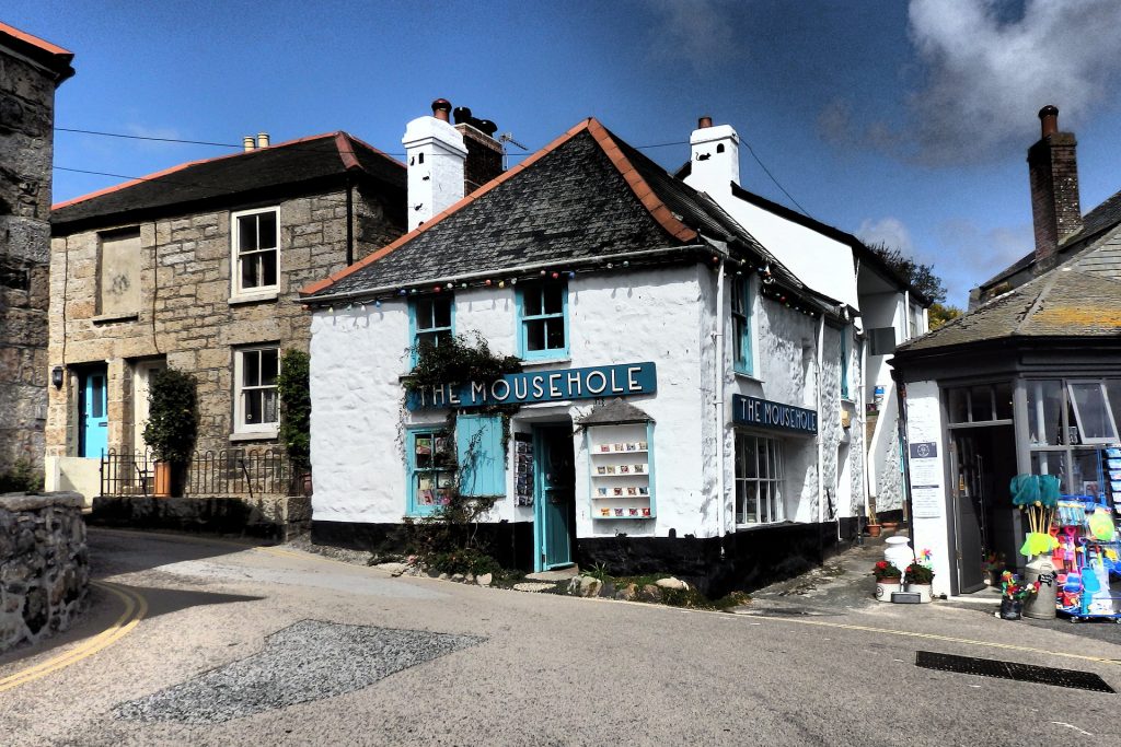 A little white house with a sign saying mousehole selling postcards outside
