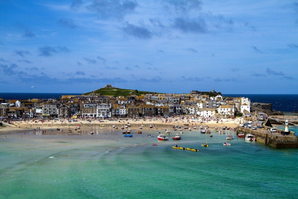 A view over st ives bay. A blue body owater meets a sandy harbour. There are boats in the water